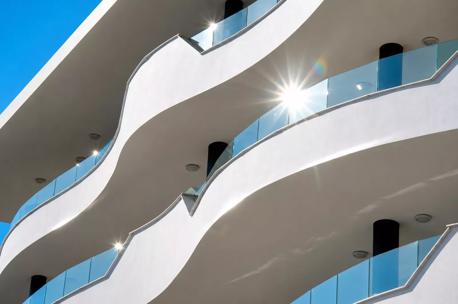 Curved balconies with glass railings against a blue sky at HW3