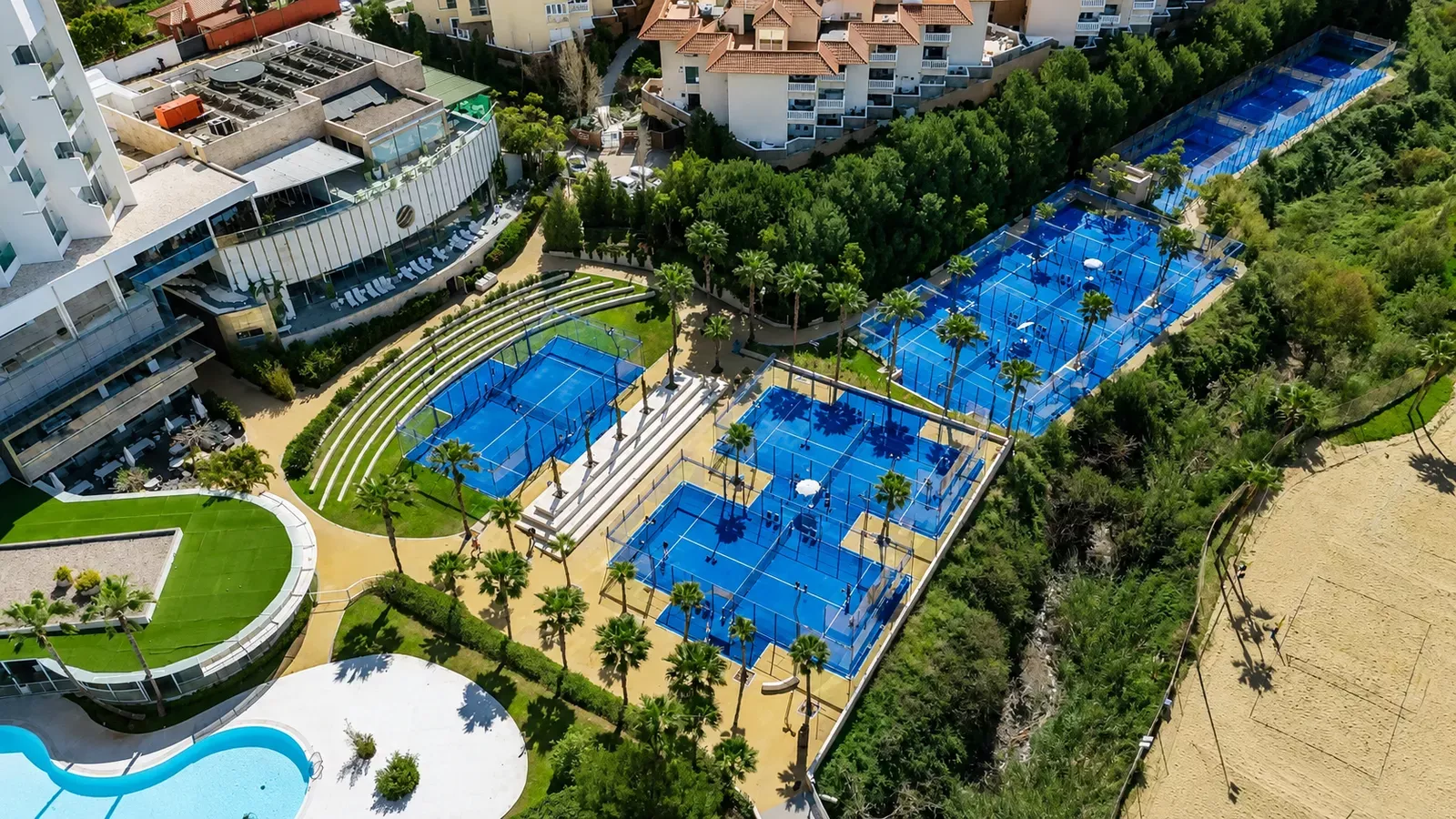 Resort seen from above with blue padel courts and a lagoon-style pool