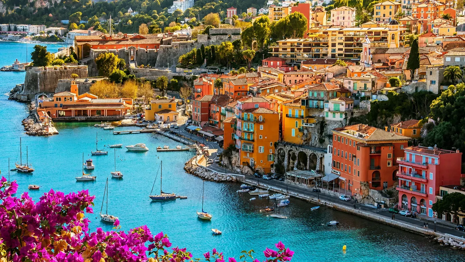 Colourful Mediterranean harbour town with boats and pink flowers in the foreground