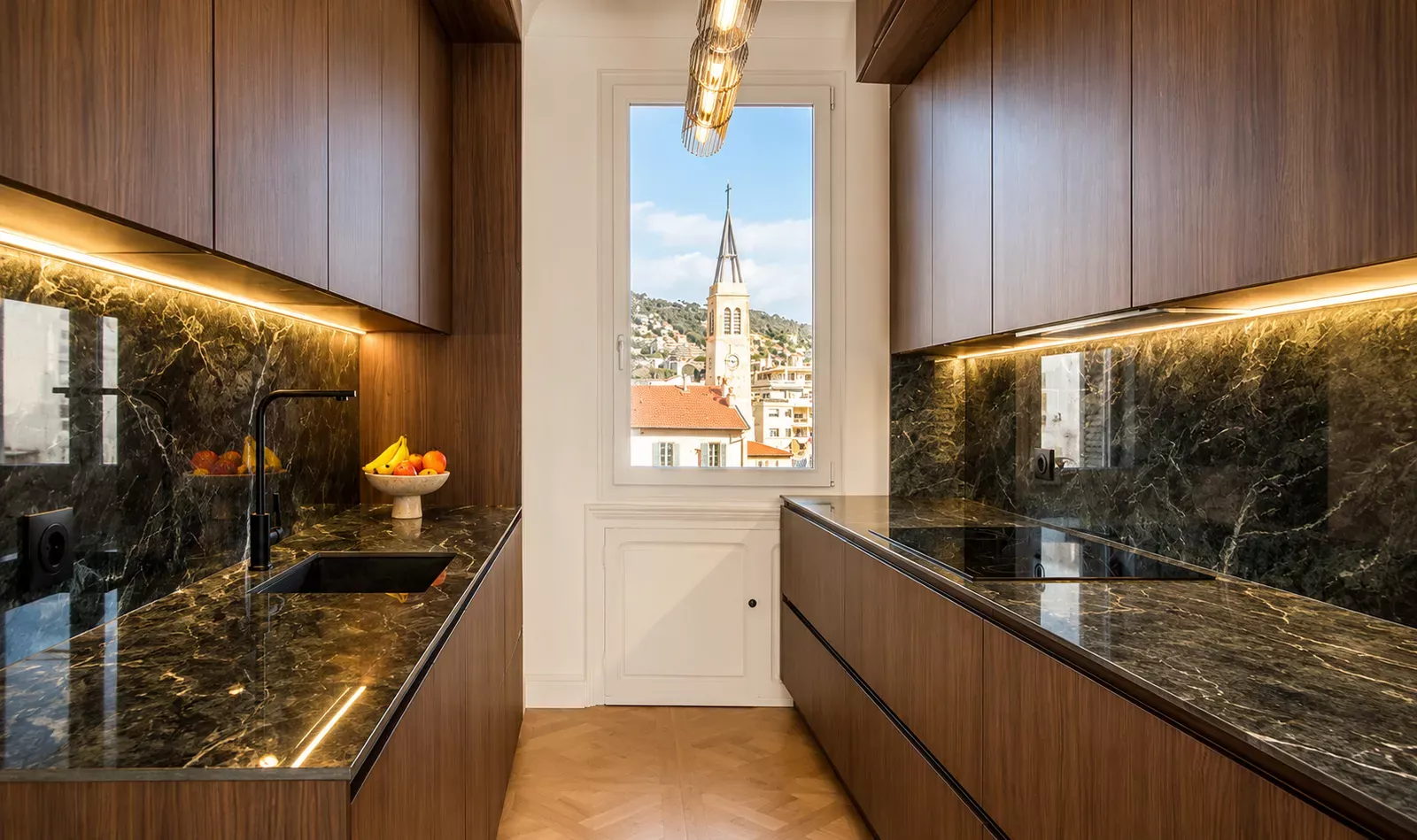 Kitchen with dark stone worktop and wooden cabinets, a church tower in the window