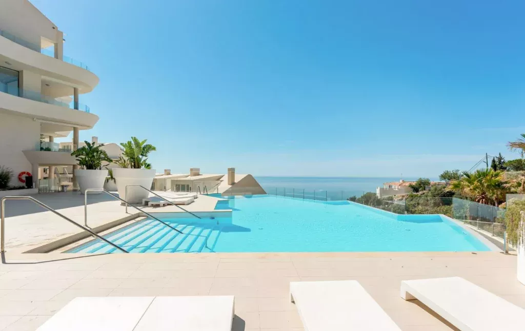 Infinity pool with loungers and the sea beside a white building at Stupa Hills