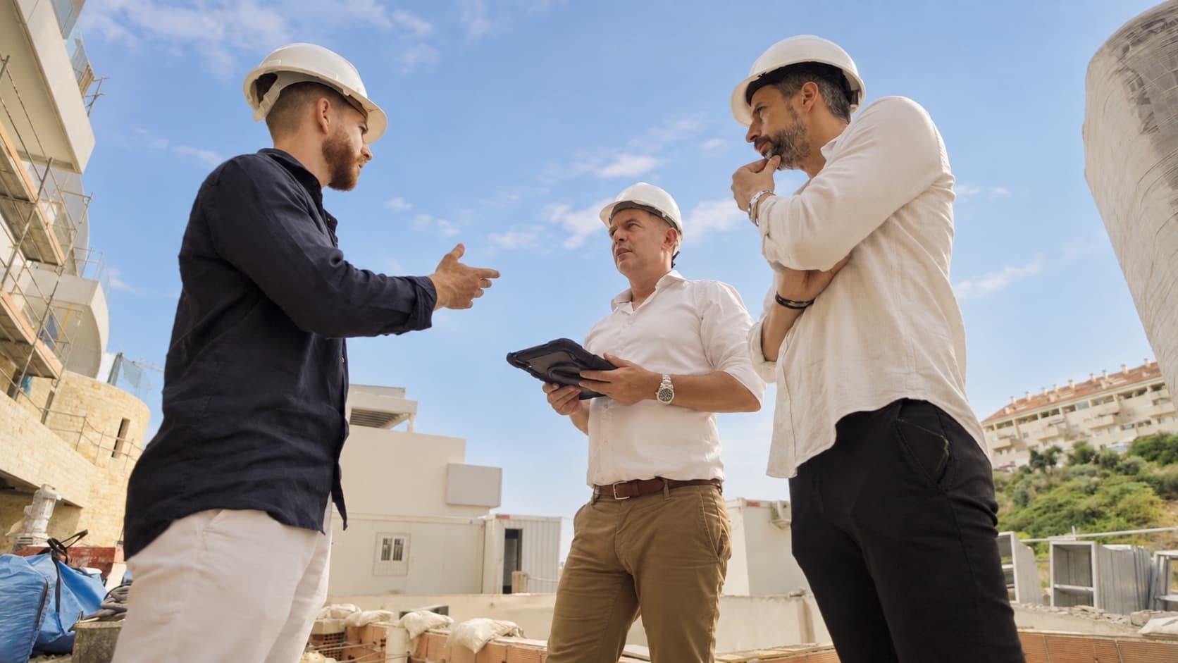 Three people in hard hats reviewing plans at a five2one construction site